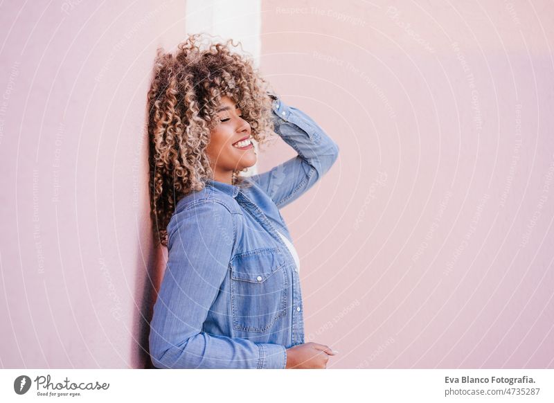 portrait of confident curvy hispanic woman outdoors in spring. pink wall. Body positivity body positivity size happy afro smiling city eyes closed