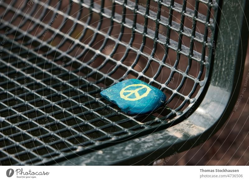 blue painted stone with yellow peace sign laying on a green metal park bench background catastrophy concept day design disaster dramatic escape freedom