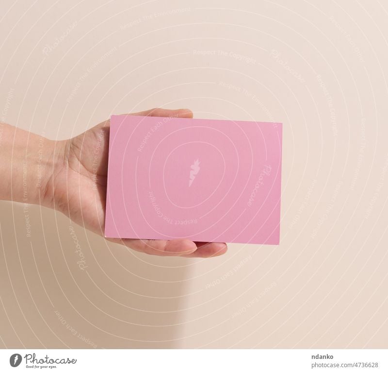 Female hand holding empty pink paper on a beige background. Copy paste image or text, close up ad adult advertise advertisement advertising announcement arm