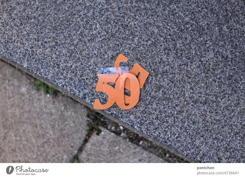 A 50 fifty in orange lies on a sidewalk.  Plastic number, number, old.  Birthday , round birthday, celebration, decoration, numbers Decoration Orange plastic