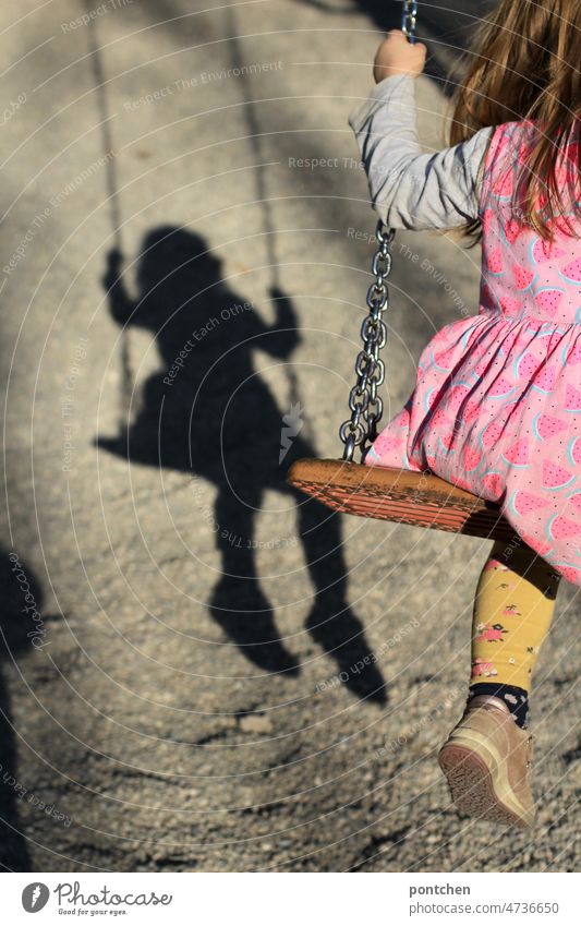 Childhood in shadows. A child on a swing casts a shadow. Burdened childhood. symbol image. Corona, pandemic Infancy To swing Shadow load corona