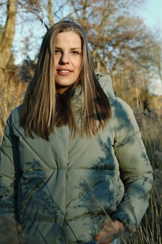 Tall blonde woman with long hair in warm light green jacket smiling very close to camera outside Landscape trees Grass Looking into the camera 18 - 30 years