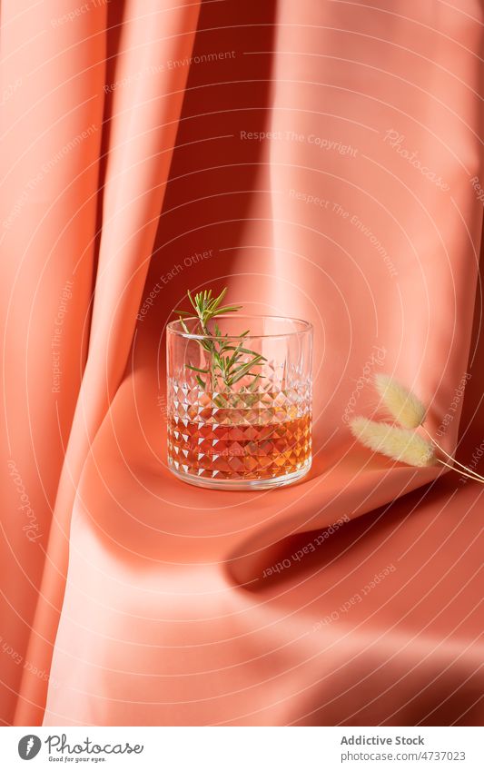 Glass of cold whiskey served with rosemary sprig on fabric glass aromatic alcohol elegant booze drapery silk twig still life lagurus beverage crystal fragile