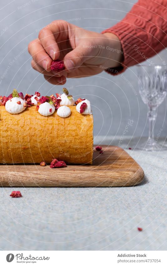 Woman adding dried raspberry on roll on wooden board woman cake dessert sweet serve cream homemade recipe female baked sugar food topping culinary table whipped
