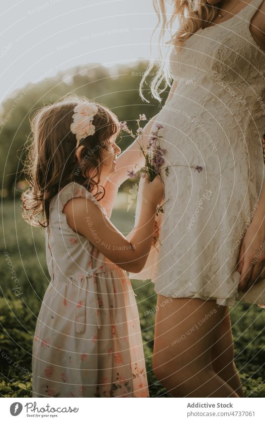Crop pregnant woman and daughter with bouquet in summer nature mother girl pregnancy child mom flower fondness await together park happy bonding maternal kid