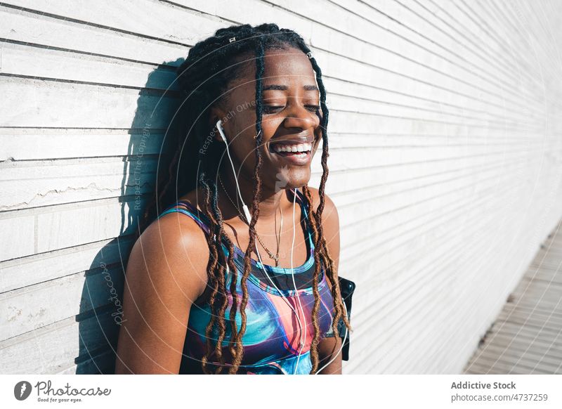 Cheerful black woman in sportswear enjoying music in earphones listen fitness workout playlist leisure happy laugh female training positive activewear sporty