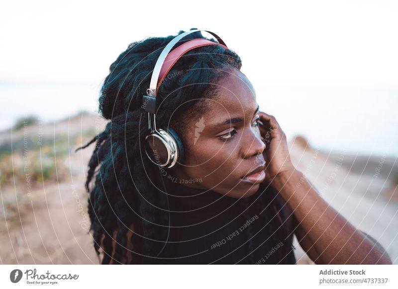 Carefree black woman listening to music on beach song headphones summer serious seashore female concentrated ethnic african american carefree freedom enjoy