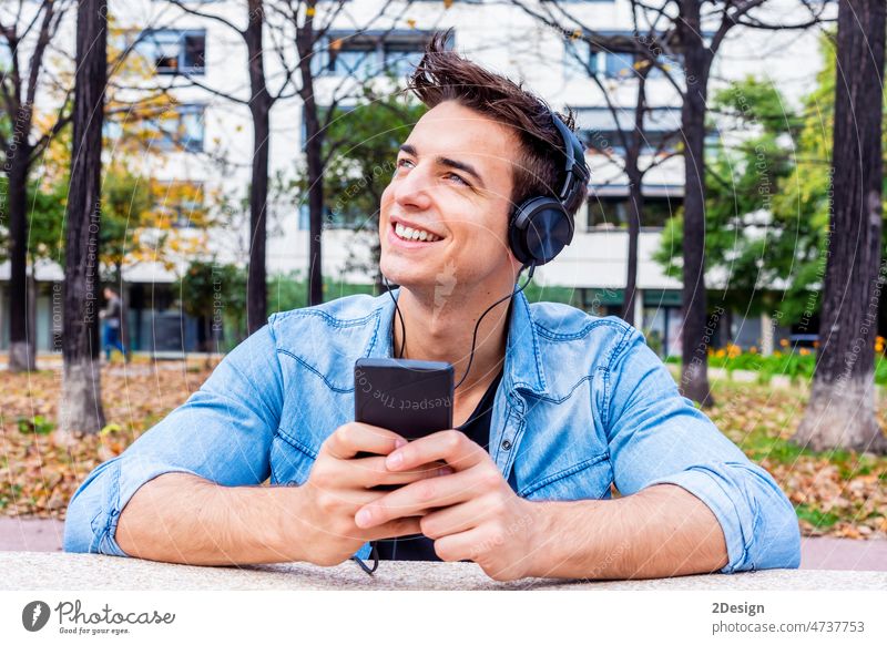 Young man enjoying music by headphones at the public park person mobile sitting bench young lifestyle male smiling earphones happy daydreams listening outdoor