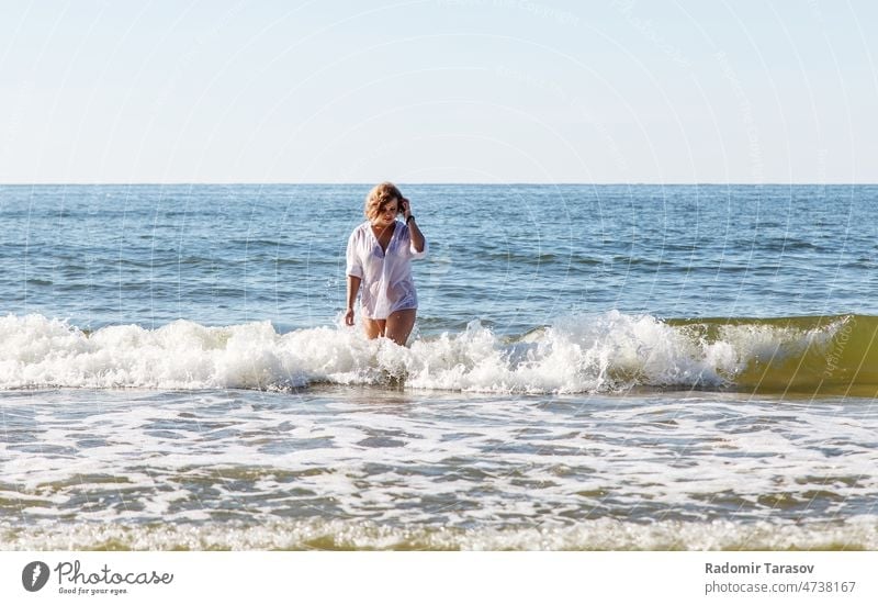 young blonde woman in a wet white shirt comes out of the water near the seashore outdoor female waves person summer hair nature happy sky relaxation