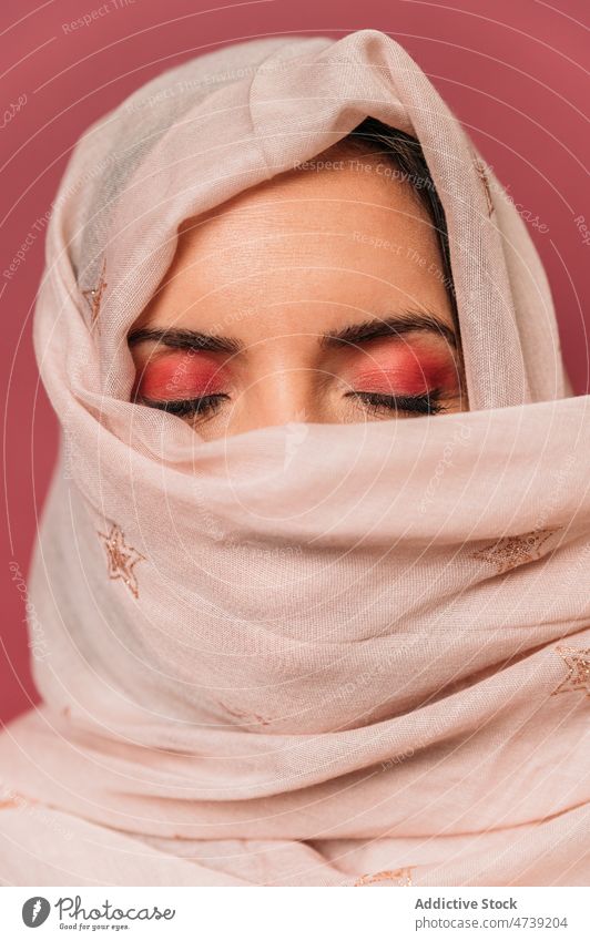 Attractive muslim woman in headscarf in studio pink style makeup feminine design cover face enigma hide trendy appearance calm eyes closed female attractive