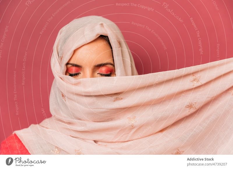 Attractive muslim woman in headscarf in studio pink style makeup feminine design cover face enigma hide trendy appearance calm eyes closed female attractive