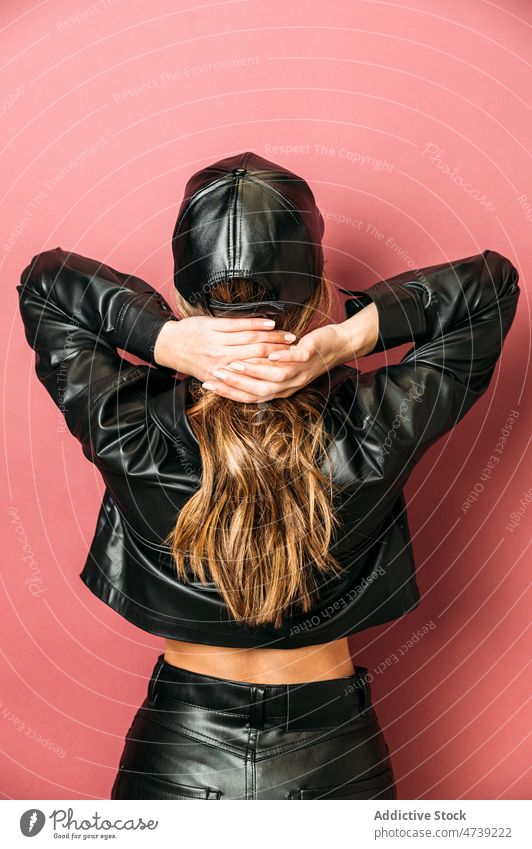 Woman posing on red backdrop woman leather jacket cap trendy style studio individuality appearance model portrait female outfit posture fashion vogue arm raised