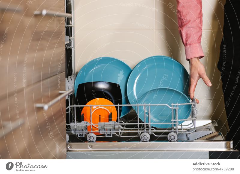 Crop man putting ceramic plates into dishwasher in kitchen load dishware equipment household housework hygiene kitchenware modern male shirt duty utensil