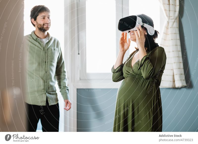 Happy pregnant couple wearing VR goggles standing near happy husband virtual reality relationship amazed explore vr smile together cyberspace digital innovation