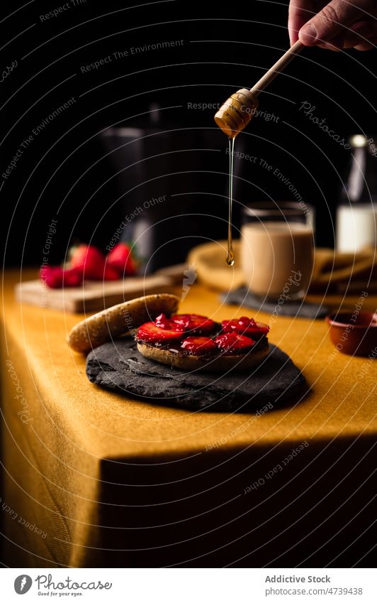 Person adding honey from wooden spoon to bagel person strawberry breakfast sweet fresh yummy chocolate serve smear coffee moka pot dessert delicious prepare