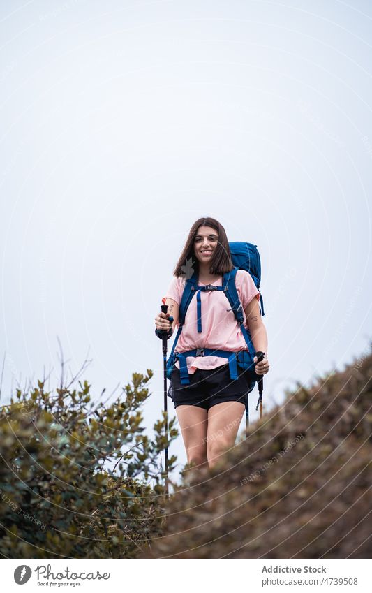 Cheerful woman with trekking poles in nature hiker adventure journey backpack activity explore female summer positive backpacker stick tourist cloudless active