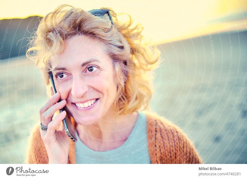 Young mature blonde caucasian woman talking with a mobile phone outdoor in a beach. Lifestyle concept. lifestyle women communication wireless technology