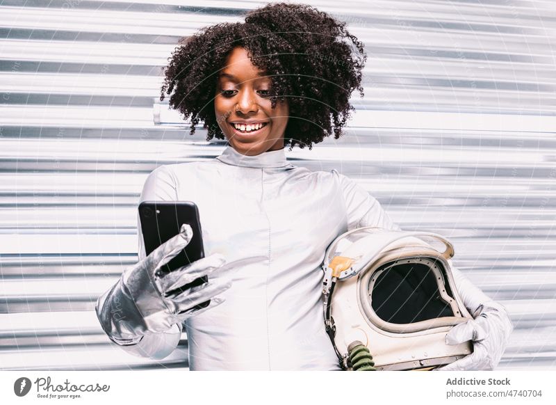 Happy black astronaut browsing smartphone in spaceship woman spacesuit helmet cosmonaut happy glad online internet surfing smile mission delight uniform modern