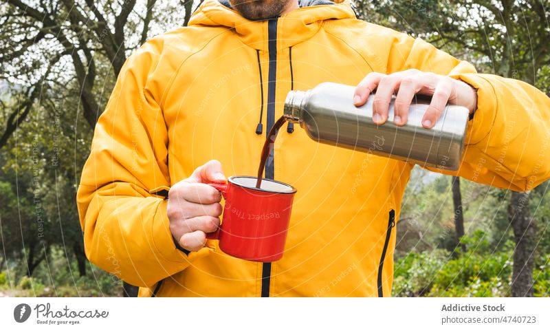 Anonymous man pouring coffee in nature thermos hot drink hiker trekking journey forest beverage explore trip woods activity adventure male explorer environment
