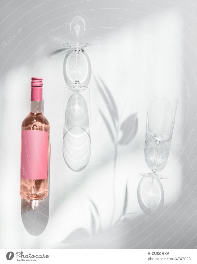 Rose wine bottle and two wine glasses at white background with sunlight rose wine empty pink mock up label shadow modern wine concept top view copy space clean