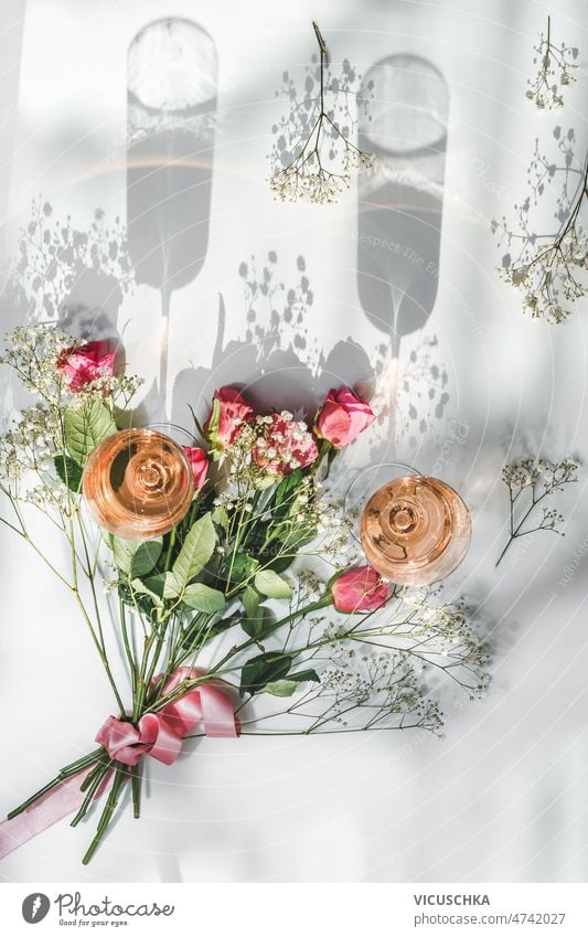 Champagne glasses with rose wine and beautiful flower bouquet with roses two champagne glasses white background sunlight shadows celebration drinks top view