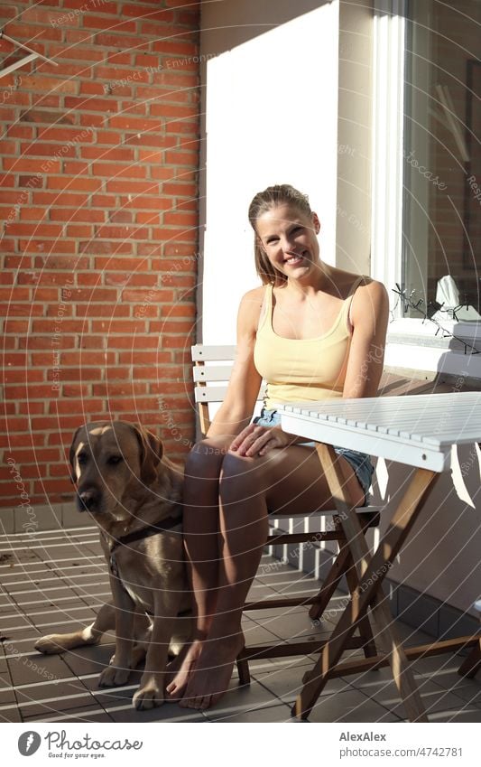 Young tall woman sitting barefoot on balcony with blonde labrador by her side Woman Large pretty Slim Athletic Esthetic fit Complexion hot pants tank top