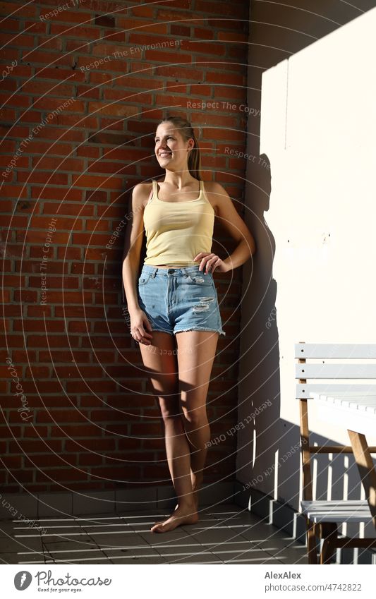 Young tall blonde woman standing on balcony barefoot in the sun leaning against brick wall Self-confident Personality Lifestyle Youthfulness Intensive Skin