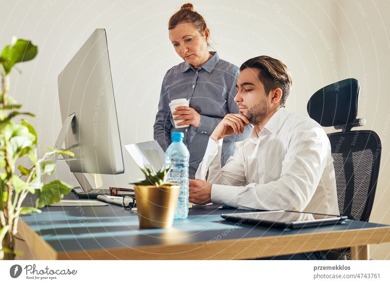 Two business people discussing financial data on computer. Businesswoman working with male colleague in office. People entrepreneurs working with charts and tables on screen. Two people working together