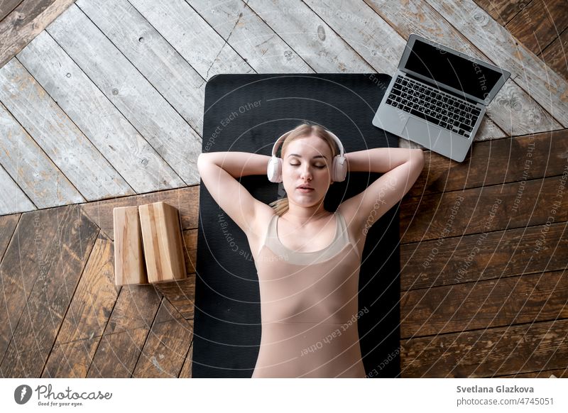 Woman closed eyes lies on sports mat on floor. Wearing headphones listening music meditation Mental Health care Wellness Yoga Myofascial relaxation woman