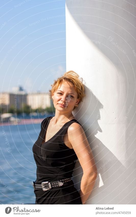 Portrait of a young girl with a short haircut. A girl on a sunny day poses on the embankment in a black dress. portrait of a girl blonde emotions attractive