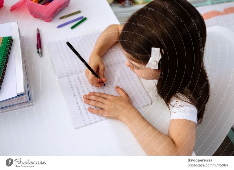 Girl doing homework sitting at a desk girl applied school at home drawing notebook homeschooling writing concentrated cute child top view overhead room studying