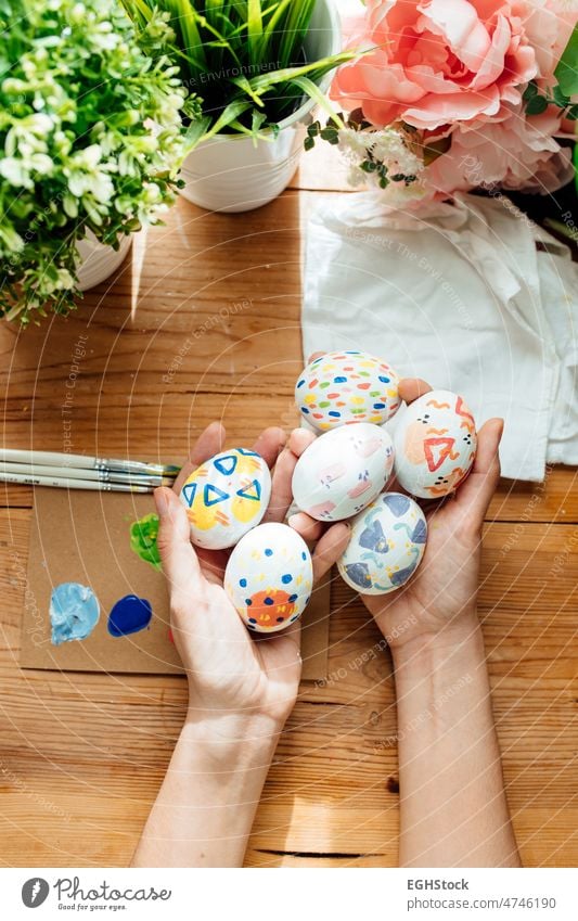 Female holding a modern easter eggs. Brushes and paints with flowers and plants. Happy easter concept on a wooden background. female hand celebration holiday