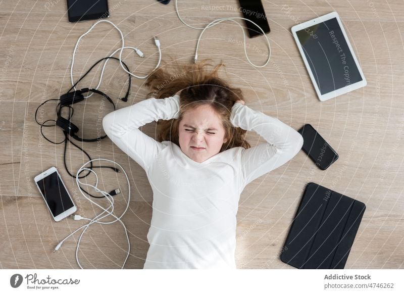 Upset girl amidst various gadgets upset cable dependency addiction punishment sad unhappy prohibit modern problem device kid smartphone tablet cellphone wire