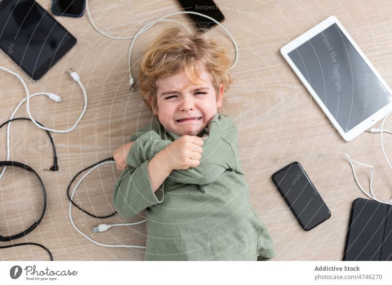 Crying boy amidst various gadgets cry upset cable dependency addiction punishment unhappy prohibit modern problem device kid smartphone tablet cellphone wire