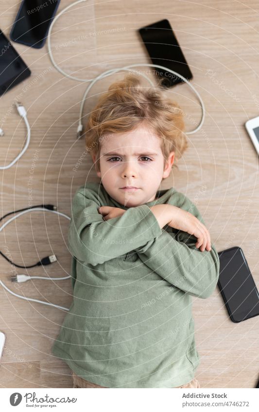 Upset boy amidst various gadgets upset cable dependency addiction punishment sad unhappy prohibit modern problem device kid smartphone tablet cellphone wire usb