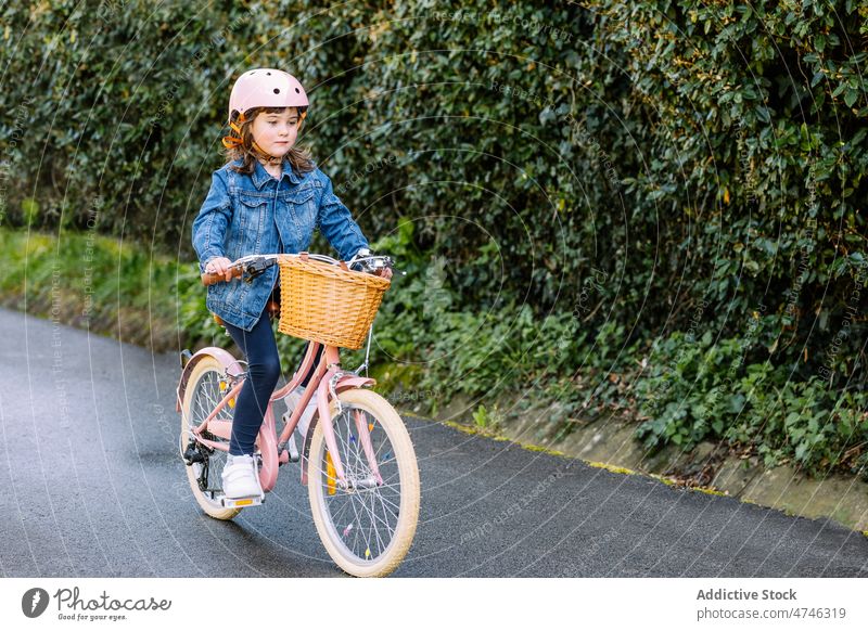 Girl riding bicycle in park girl kid hobby leisure pastime childhood transport helmet path focus basket activity summer bike tree safety concentrate summertime