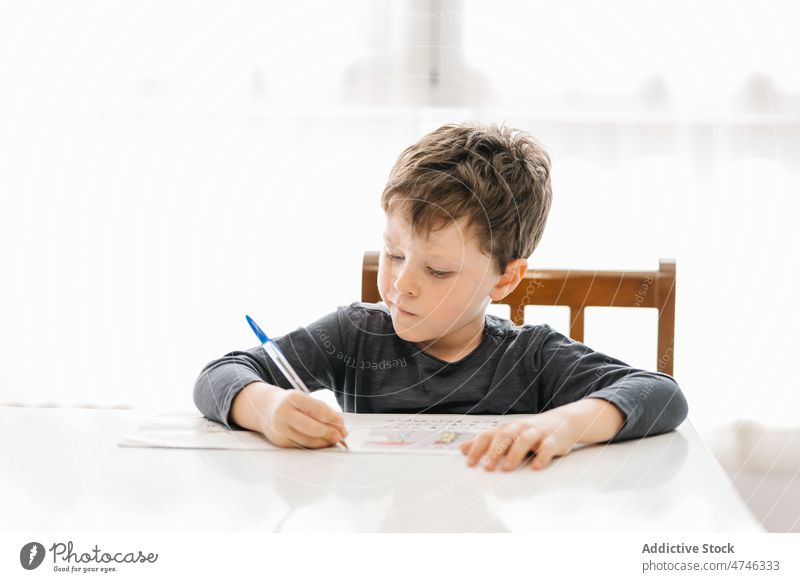 Boy writing on paper at table kid boy study write homework knowledge education primary cognition smart diligent desk focus take note task concentrate at home