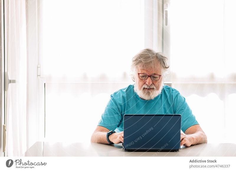 Elderly man with laptop at home browsing spare time weekend using gadget device internet online focus house netbook attentive watching male free time room sit