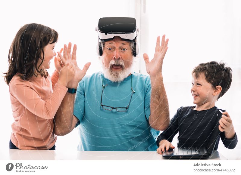 Astonished grandfather in VR goggles near children vr explore cyberspace futuristic immerse laptop astonish having fun virtual reality netbook simulator modern