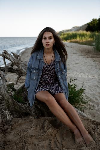 A fashionable girl dressed in blue jeans and a summer dress is looking straight into the camera. A picturesque background of Golden Dunes in Nida, Lithuania. It’s not that hard to feel the summer breeze in this one.