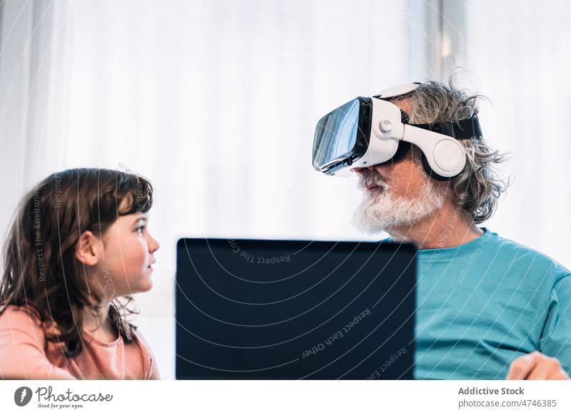 Grandfather in VR headset playing videogame near girl grandfather vr explore cyberspace futuristic immerse virtual reality laptop netbook browsing simulator