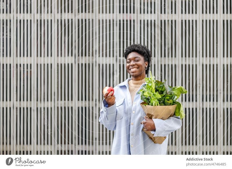 Content black woman with bag of groceries eating apple street greens healthy food organic smile vitamin nutrition grocery fruit happy purchase city fresh female