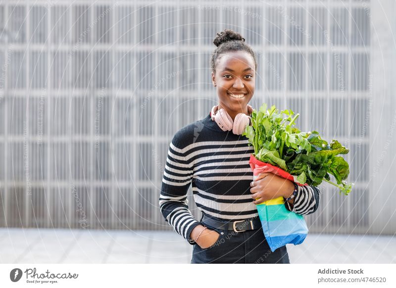 Delighted black woman with green at wall headphones street greens beetroot smile healthy food organic vitamin nutrition metal wall bag happy wireless meloman