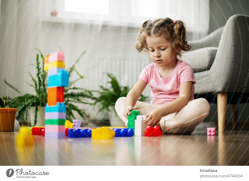 A little girl is sitting on the floor in the playroom and playing with colorful cubes, a constructor. child construction blocks build beautiful kindergarten