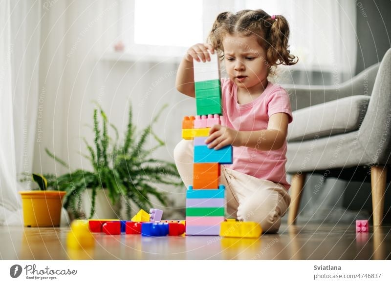 A little girl is sitting on the floor in the playroom and playing with colorful cubes, a constructor. child construction blocks build beautiful kindergarten