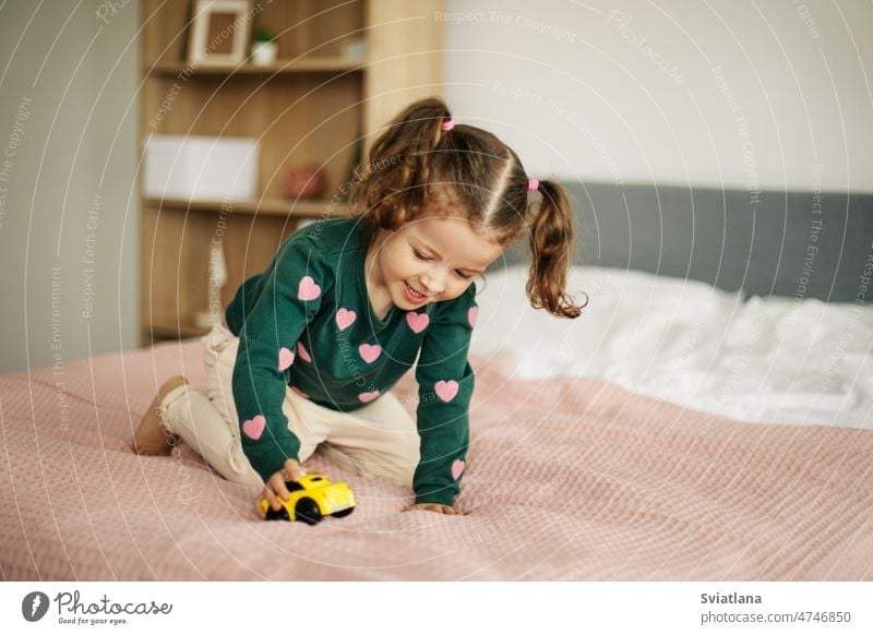 A charming little girl is playing with a car on the bed. Home games, child development home games baby toys cute children background small family beautiful