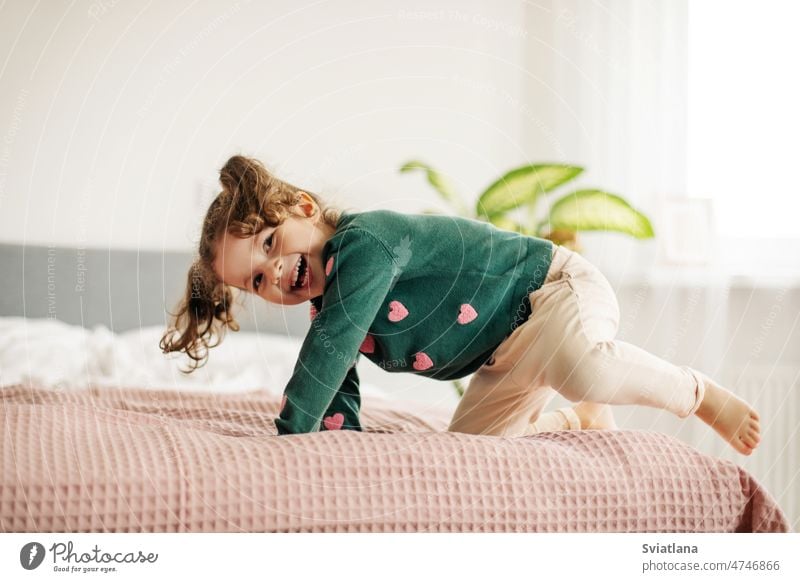A charming little girl jumps on the bed and laughs fun female cute child morning portrait hair indoor face emotional day cheerful caucasian beautiful happiness