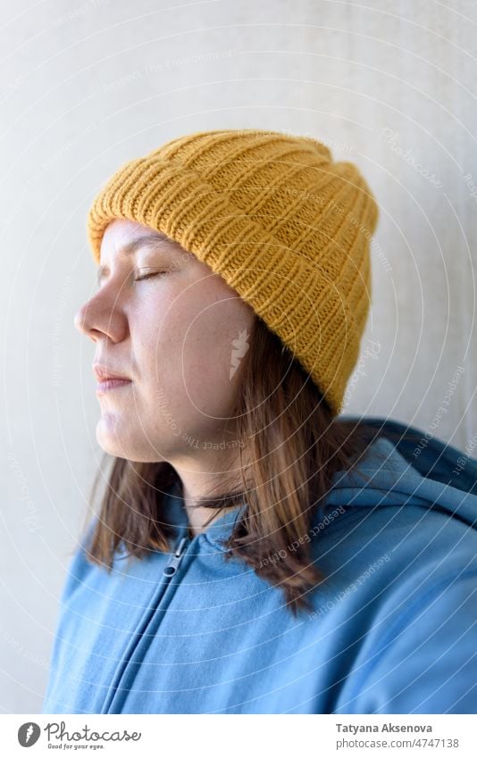 Woman in yellow hat and blue sweatshirt woman anxiety worried concern sad knitted 30s millennial eyes closed caucasian selfie authentic