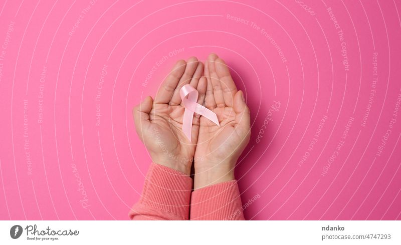 two female hands hold a pink silk ribbon in the form of a loop on a pink background. Symbol of the fight against breast cancer woman disease health person care