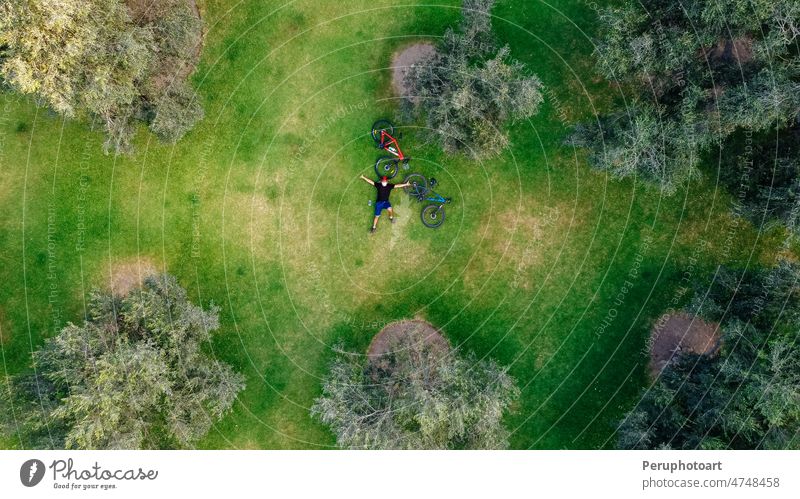 Aerial drone view of a cyclist lying down and resting in a meadow. man park biking tree enjoying bicycle above background pattern sport summer texture nature